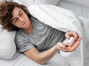 Person in bed pouring capsules from a pill bottle into their hand