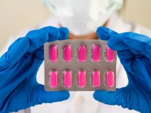 Healthcare professional in blue gloves holding a blister pack of pink tablets